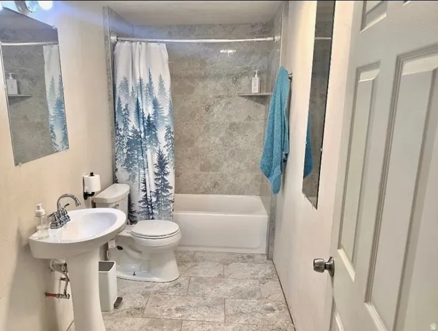 Bathroom featuring a pedestal sink, white toilet, and a bathtub with a tiled surround