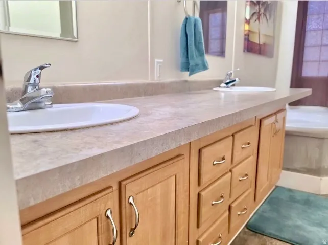 Double vanity with two integrated sinks, light-toned countertop, and natural wood cabinetry featuring brushed nickel hardware