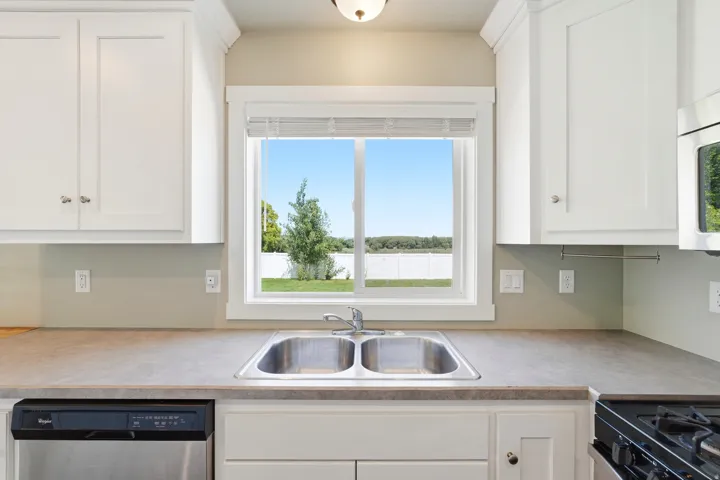Kitchen featuring white cabinetry with silver hardware, a stainless steel double-basin sink, and gray countertops