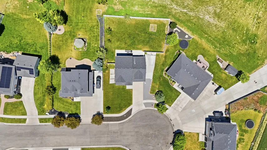 Overhead perspective featuring a property with a dark shingle roof, concrete driveway, and established landscaping