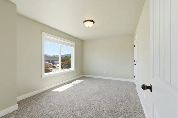 Bright room featuring a large window with white blinds, carpet flooring, light-toned walls, and a ceiling-mounted light fixture