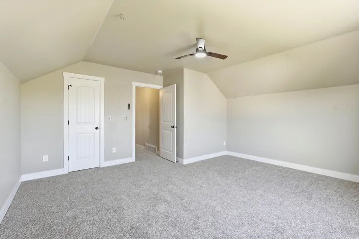 Spacious room featuring gray textured carpeting, neutral wall finishes, and a contemporary ceiling fan with integrated lighting