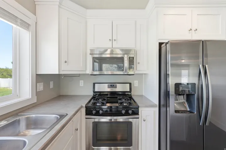 Kitchen featuring white cabinetry, stainless steel appliances including a gas range and side-by-side refrigerator, a double-basin stainless steel sink, and light-toned countertops