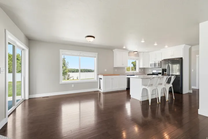 Open-concept kitchen and living area featuring dark wood-finish flooring, white cabinetry, a central island, and a sliding glass door