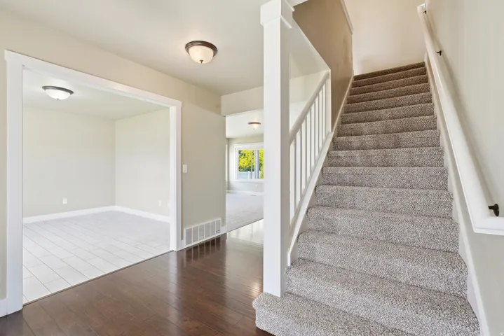 Entryway featuring rich wood-finish flooring, a carpeted staircase with white railings, and an open doorway leading to a room with light-toned tile flooring