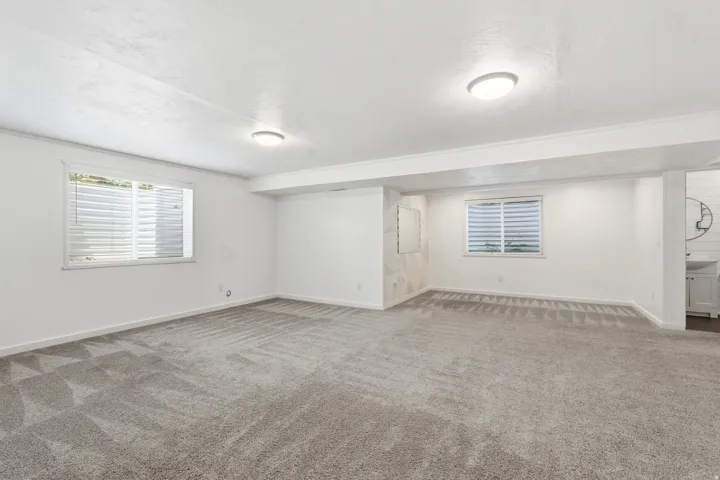 Spacious interior room featuring light gray patterned carpeting and two windows with horizontal blinds