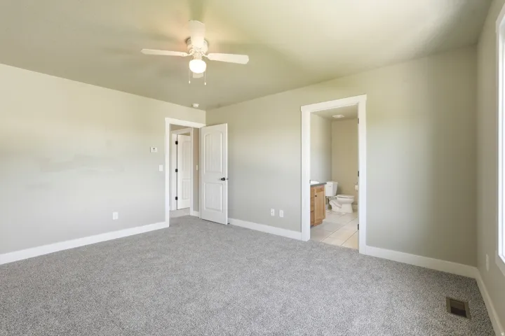 Spacious room featuring light gray carpet flooring, neutral painted walls, white baseboards, and a ceiling fan with integrated lighting