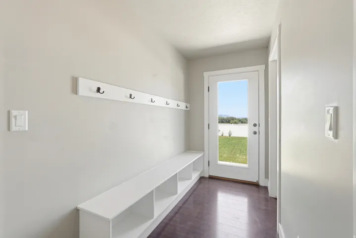 Entryway mudroom featuring a built-in storage bench, wall-mounted coat rack with black hooks, and wood-finish flooring