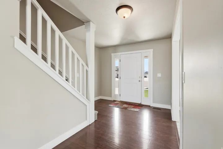 Entryway featuring wood-finish flooring, a white paneled entry door with sidelight windows, and a staircase with white balusters