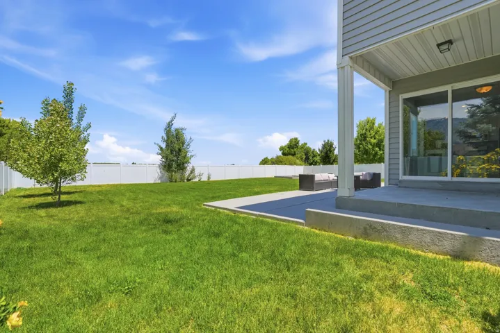 Expansive rear yard featuring a concrete patio, exterior lighting, a full vinyl privacy fence, and mature trees