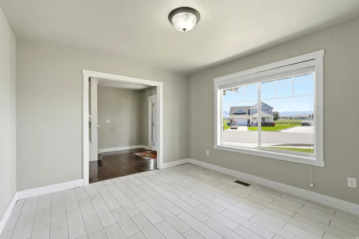 Spacious room featuring light-toned wood-finish flooring, a large window with blinds, and neutral wall paint