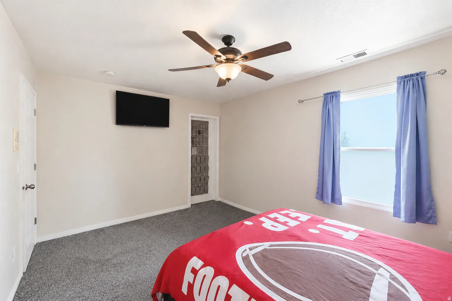 Carpeted interior space featuring a ceiling fan with integrated lighting, a window with a white frame, and a white door with a black handle