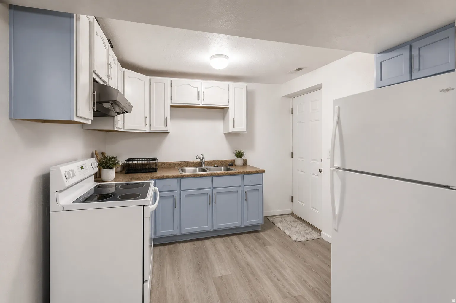 Kitchen featuring white appliances, a range hood, a double basin sink, light wood-finish flooring, and two-tone cabinetry with light blue lower cabinets