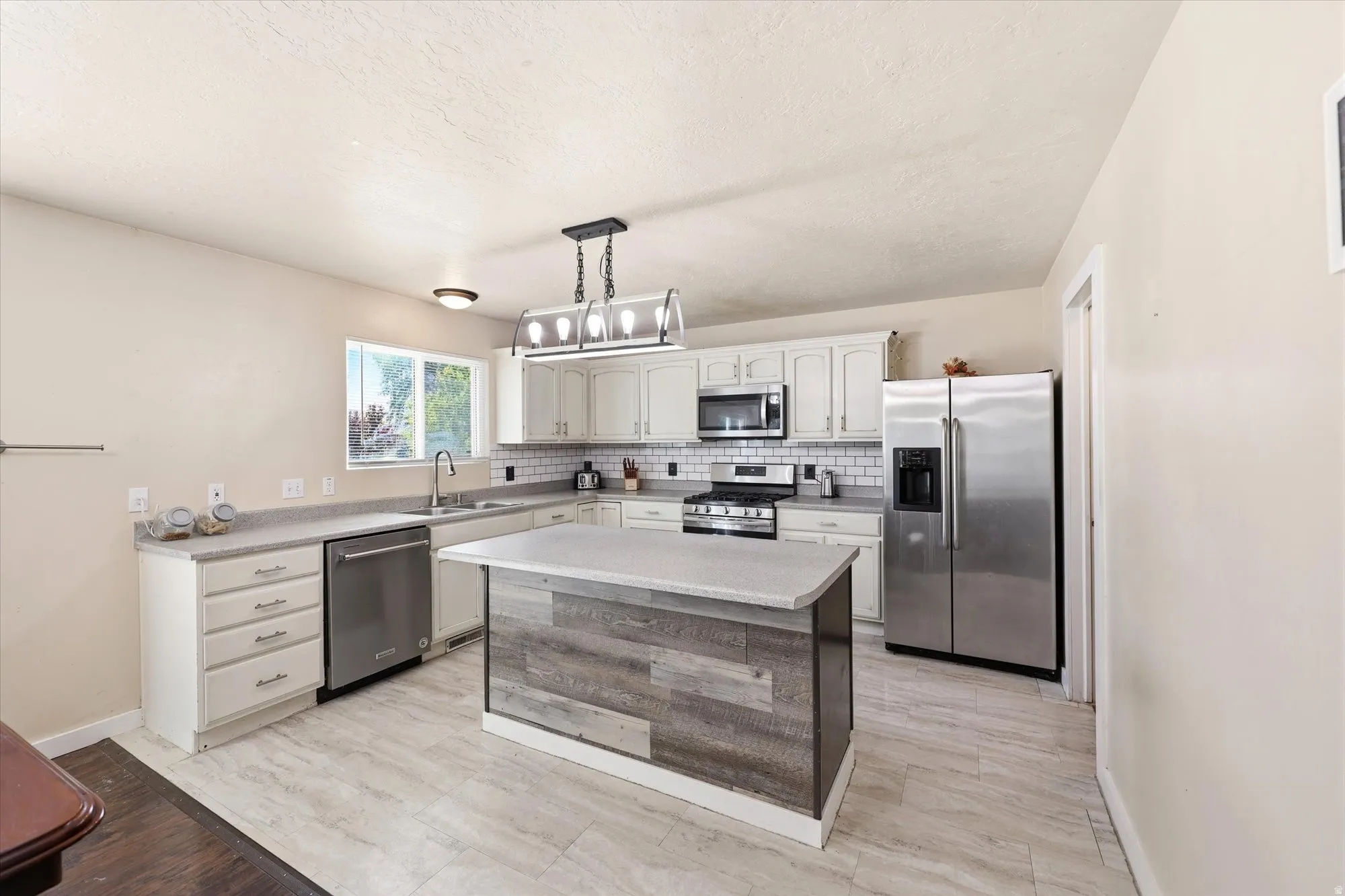 Kitchen featuring light wood-finish flooring, white cabinetry, a wood-panel island with a light countertop, stainless steel appliances, and a subway tile backsplash