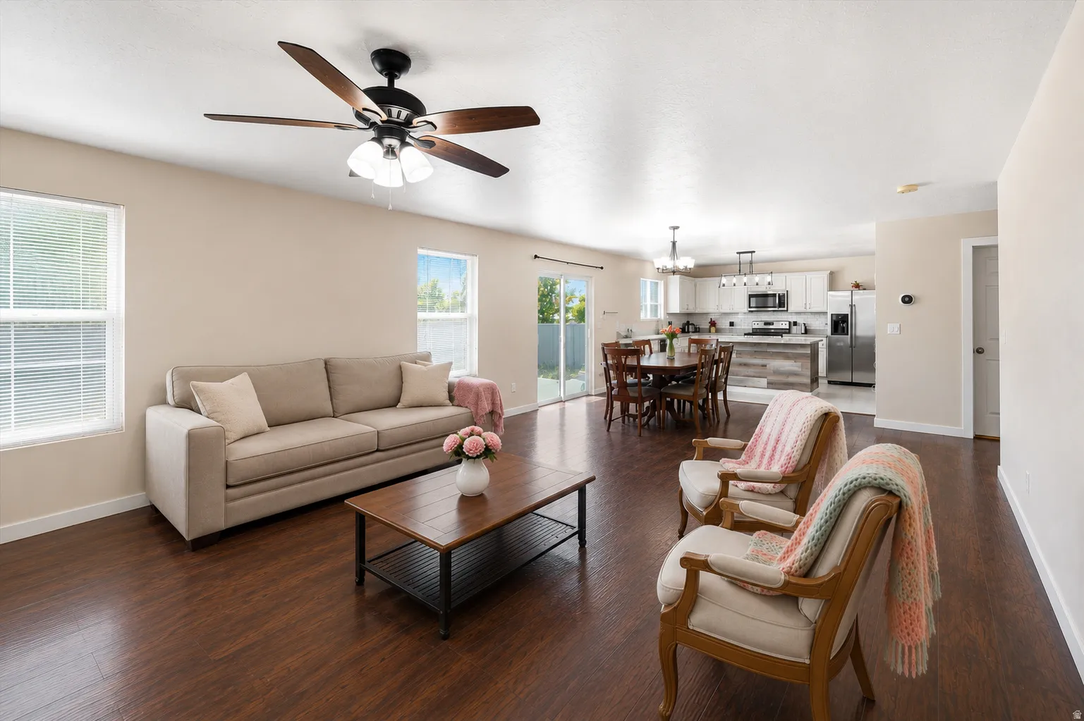Open-concept living area featuring wood-finish flooring, a contemporary ceiling fan, and multiple windows with white blinds