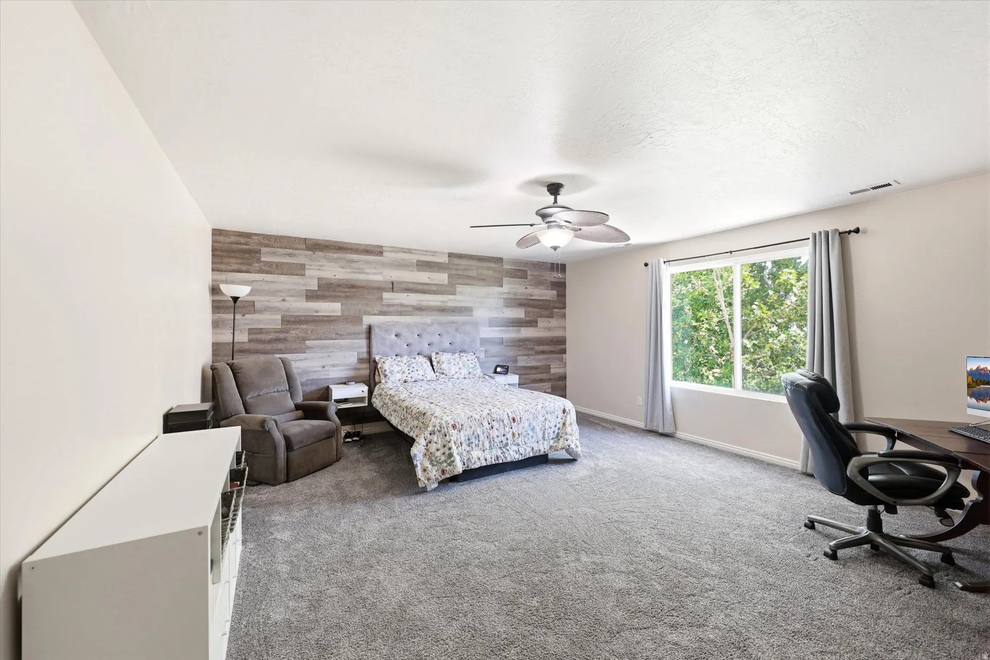 Spacious room with plush gray carpeting, a decorative wood-panel accent wall, and a large window