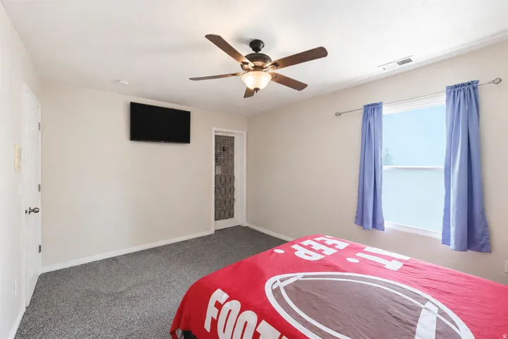 Carpeted interior space featuring a ceiling fan with integrated lighting, a window with a white frame, and a white door with a black handle