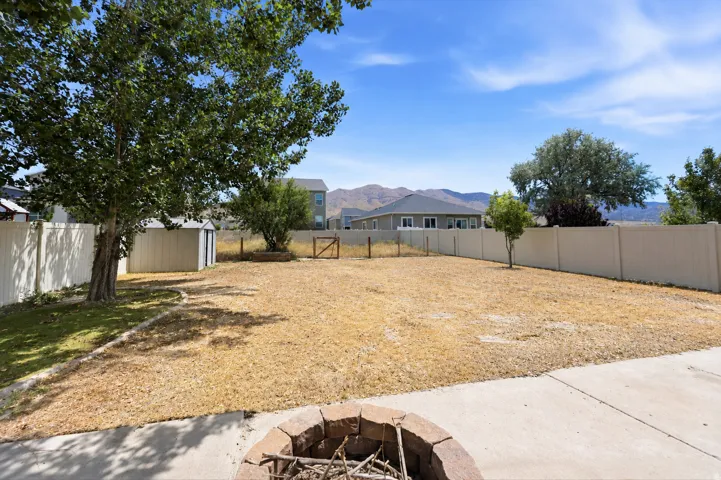 Spacious backyard featuring a stone-clad fire pit, mature trees, a storage shed, a privacy fence, and concrete patio areas
