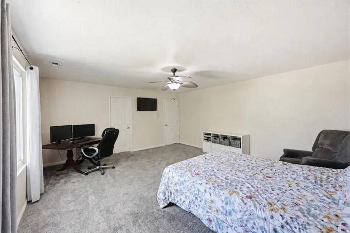 Spacious room featuring light-colored walls, grey carpet flooring, and a ceiling fan with integrated lighting