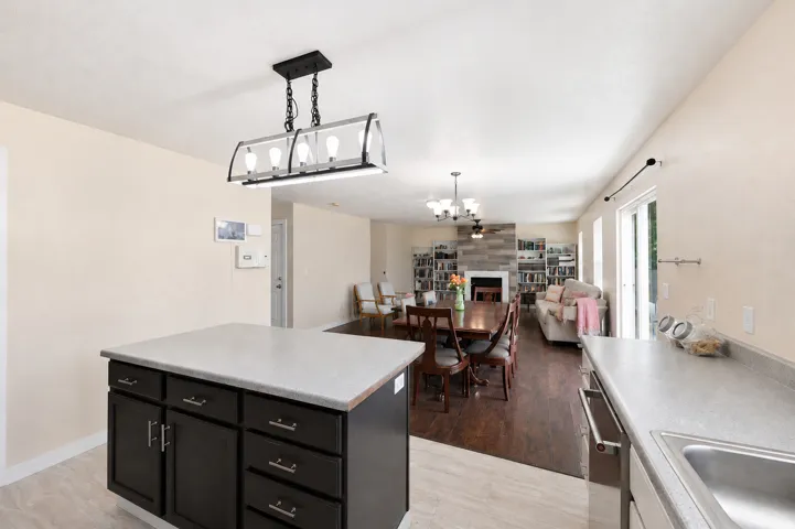 Kitchen island with dark cabinetry and light-toned countertop, featuring a linear chandelier overhead