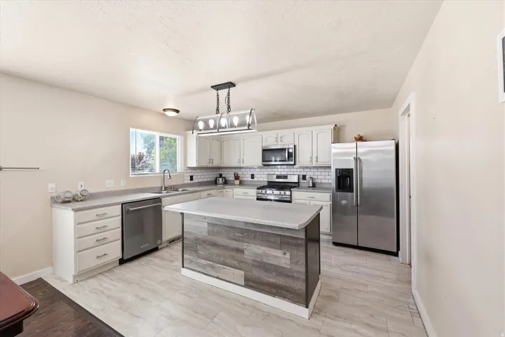 Kitchen featuring light wood-finish flooring, white cabinetry, a wood-panel island with a light countertop, stainless steel appliances, and a subway tile backsplash