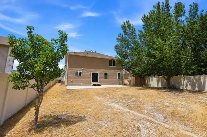 Expansive rear yard featuring mature trees, a concrete patio, and full perimeter fencing