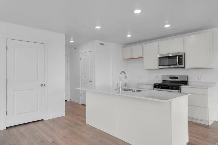 Modern kitchen featuring a white island with a stainless steel sink, white cabinetry, stainless steel microwave, gas range, and wood-finish flooring