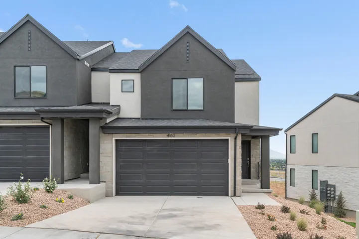 Contemporary townhouse exterior featuring a gray and white stucco facade, black framed windows, and a two-car garage
