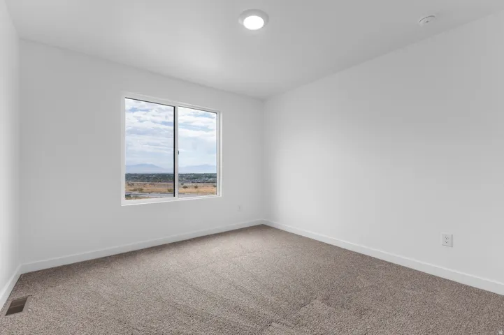 Bright room featuring a large window, plush gray carpet, clean white walls, and recessed ceiling lighting