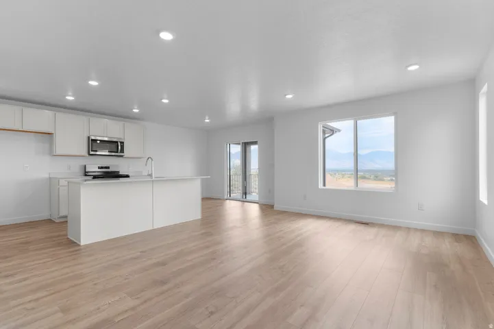 Open-concept living space with light wood-finish flooring, recessed lighting, and a kitchen island with an integrated sink