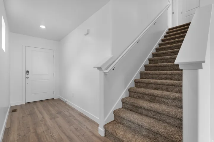 Entryway featuring light wood-finish flooring, a white paneled door, and a staircase with textured carpet
