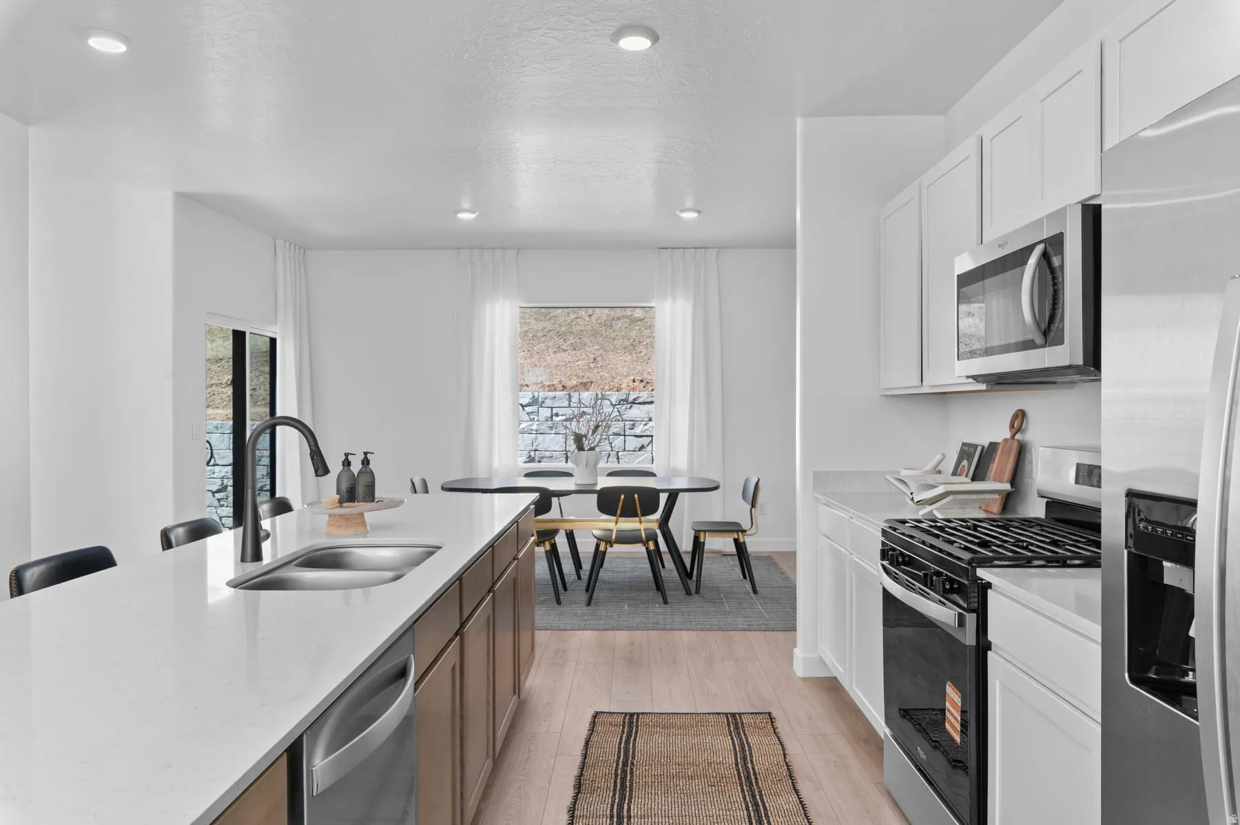 Bright kitchen featuring an expansive island with an undermount sink and matte black faucet, quartz countertops, a full suite of stainless steel appliances, and abundant white cabinetry