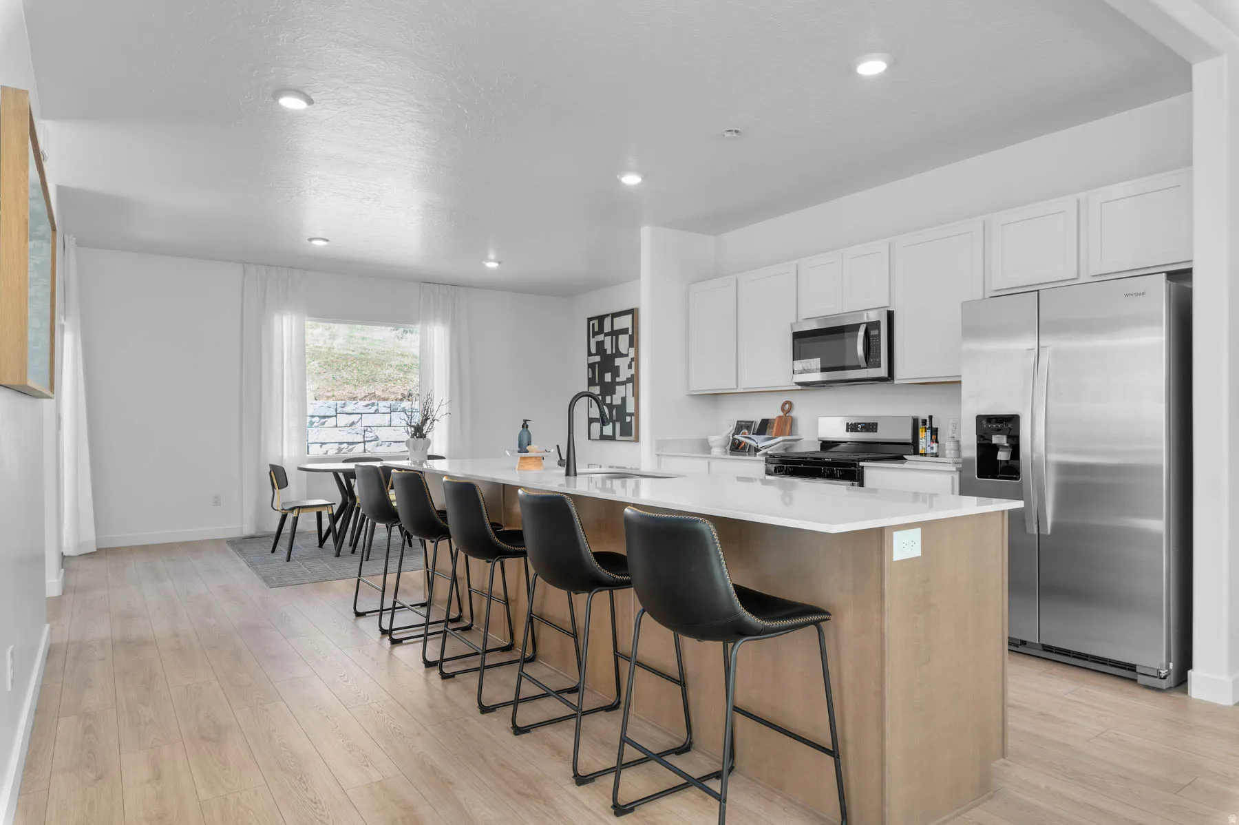 Open-concept kitchen featuring a spacious island with seating, stainless steel appliances, light wood-finish flooring, white cabinetry, and recessed lighting