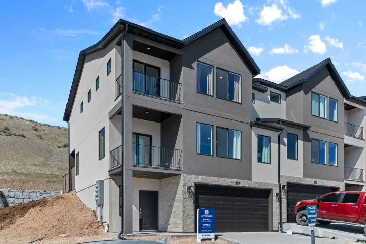 Modern townhouse exterior featuring a two-tone facade, multiple balconies with black railings, a two-car garage, and a contemporary dark entry door