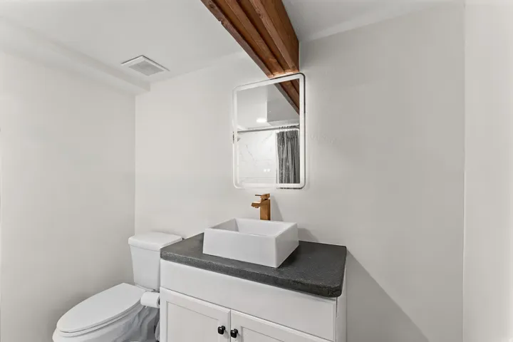 Vanity featuring a vessel sink, gold-finish faucet, and an illuminated mirror