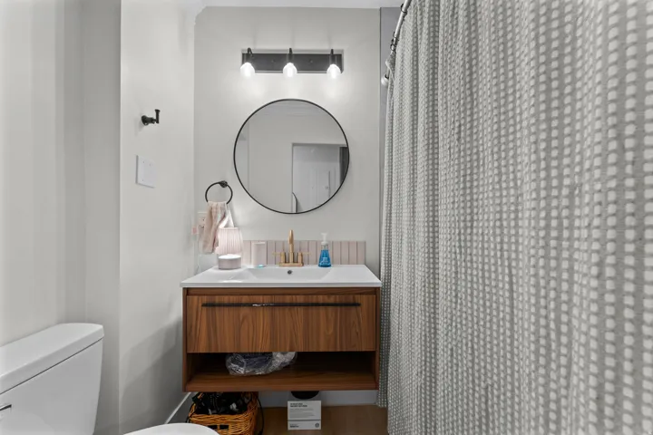 Bathroom featuring a floating wood-finish vanity with an integrated sink, a circular black-framed mirror, and a three-light matte black fixture