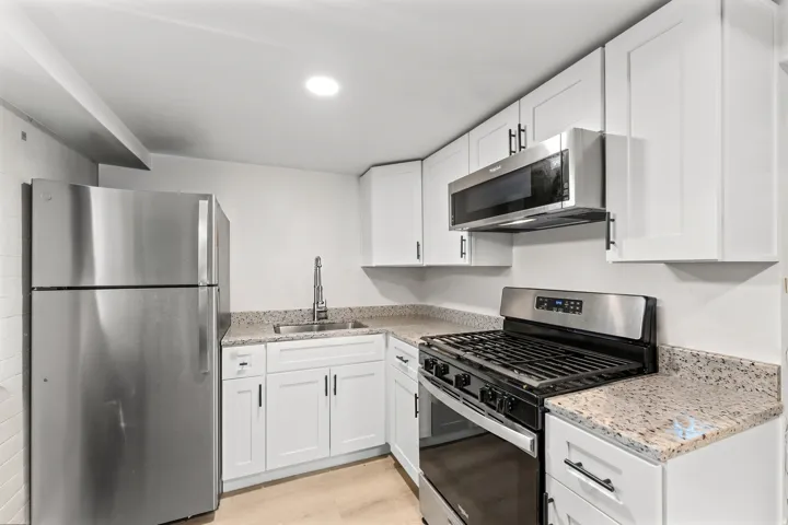 Kitchen featuring white cabinetry, light-toned countertops, stainless steel appliances, and wood-finish flooring