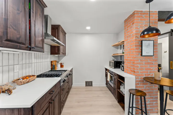 Galley kitchen featuring dark wood cabinetry, white countertops, and a full-size range with a stainless steel hood