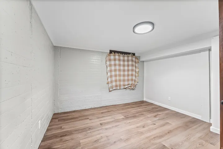 Room featuring wood-finish flooring, painted brick-texture walls, a flush-mount ceiling light, and a window opening