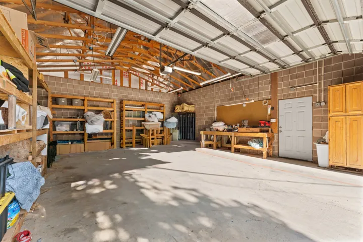 Spacious garage featuring a concrete floor, exposed wood ceiling trusses, a metal roll-up door, brick-patterned block walls, and fluorescent lighting fixtures