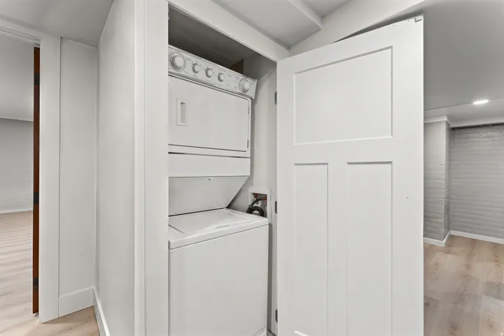 Built-in stacked laundry appliances in a dedicated closet with a white three-panel door, featuring light wood-finish flooring
