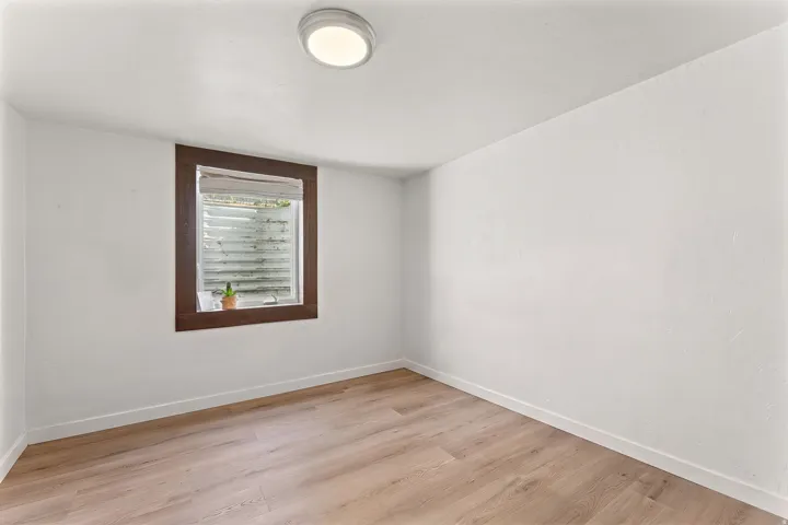 Room featuring wood-finish flooring, white walls, and a recessed window with dark wood trim