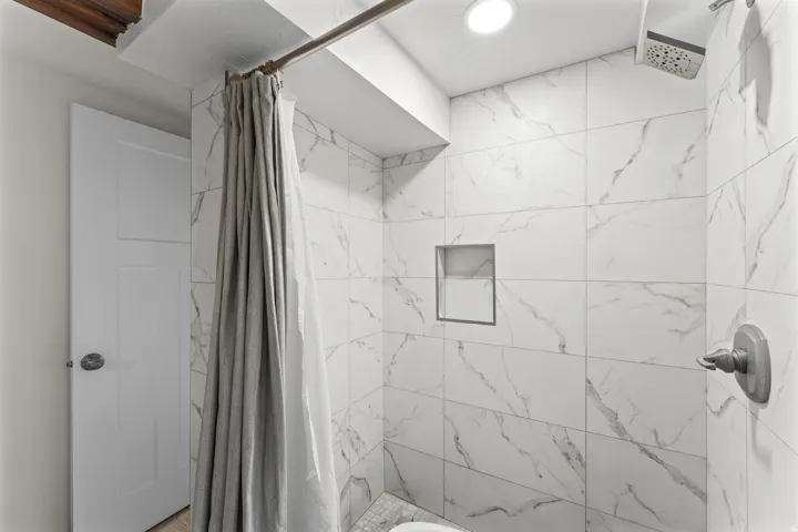 Shower enclosure featuring white tile with gray veining, a built-in shower niche, and a rain-style shower head