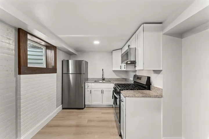 Compact kitchen featuring light wood-finish flooring, white cabinetry, and granite-style countertops