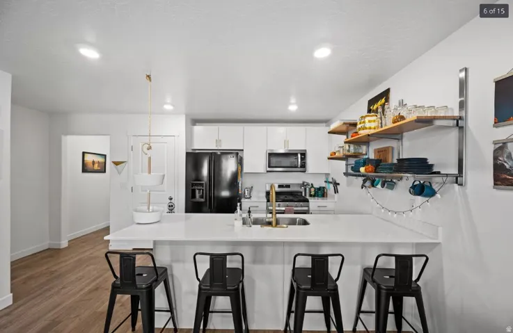 Modern kitchen featuring a white countertop island with seating, white cabinetry, integrated stainless steel appliances, and wood-finish flooring