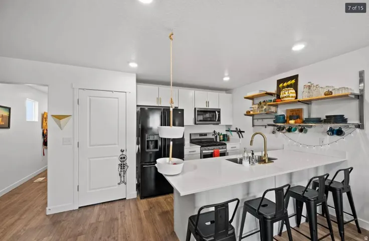 Modern kitchen featuring white cabinetry, a large center island with seating, integrated sink with a gold-tone faucet, black appliances, and contemporary wood-finish flooring