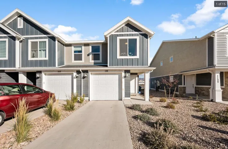 Modern townhome exterior featuring gray vertical siding, white trim accents, a single-car garage, and a concrete driveway