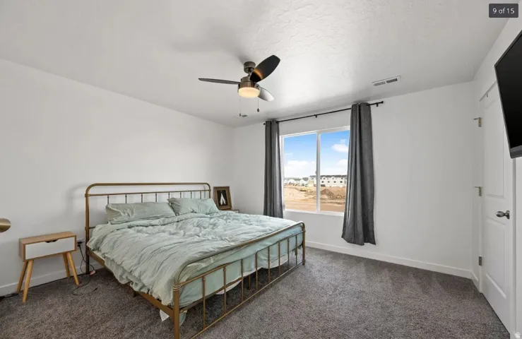 Bedroom with neutral wall tones, gray carpeting, and a ceiling fan with integrated lighting