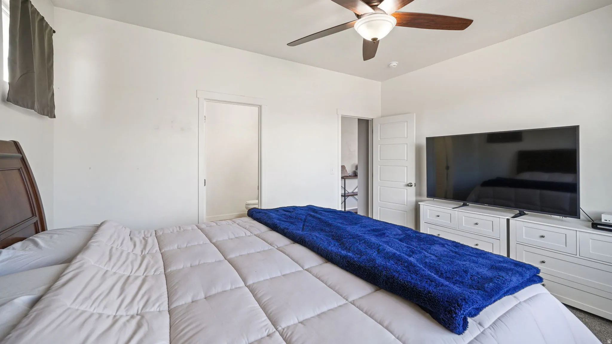 Spacious bedroom featuring a ceiling fan with integrated lighting, a white five-panel interior door, and light-toned walls