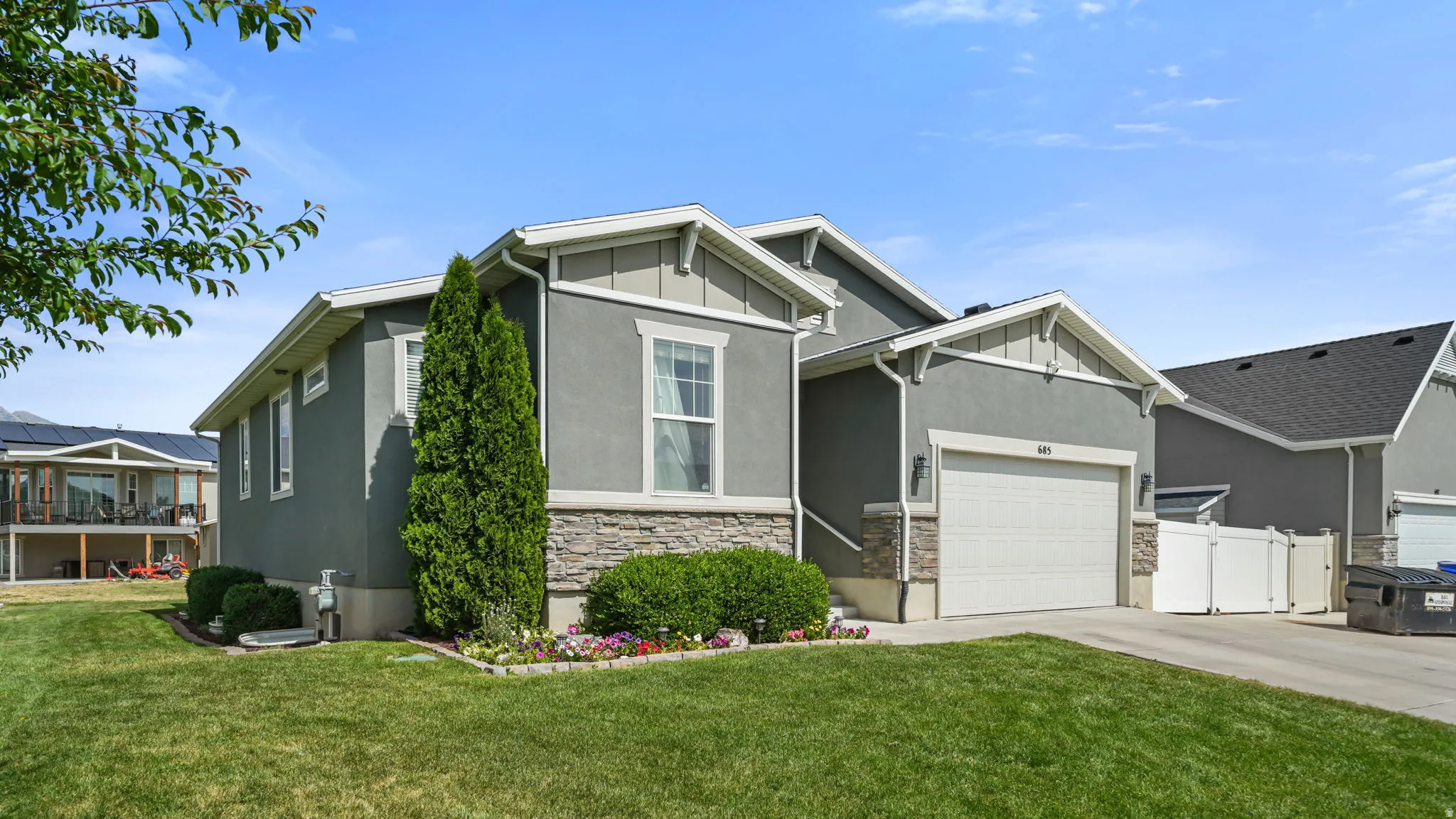 Contemporary gray stucco exterior featuring a stone accent foundation, attached garage, and manicured landscaping